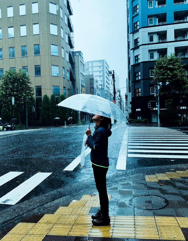 A woman standing in the rain on a city street, looking up